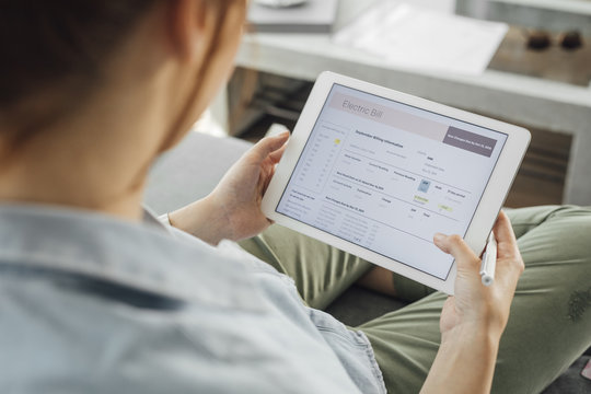 Close up of cropped unrecognisable woman reading electric bill on tablet.