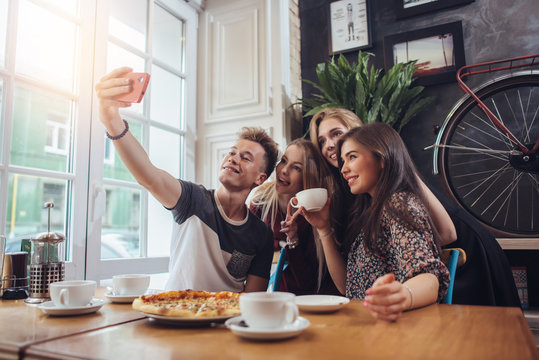 A guy taking a self-portrait with his female groupmates using his smartphone while hanging out in a coffee shop