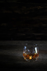 Glass of liquor on wooden floor in low light.