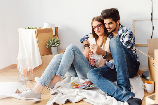 Young cheerful couple unpacking cardboard boxes and choosing color for painting new home