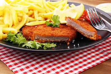 Dish of Wiener schnitzel and French fries served with sauces and salad on rustic wooden table
