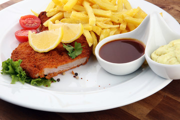 Dish of Wiener schnitzel and French fries served with sauces and salad on rustic wooden table