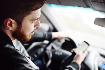 Young cute guy with a beard dials a message on the smartphone in the car