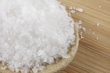 Close up of salt on wooden spoon over wooden background.