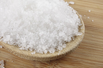 Close up of salt on wooden spoon over wooden background.