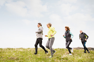 Group of seniors running outside on the green hills.