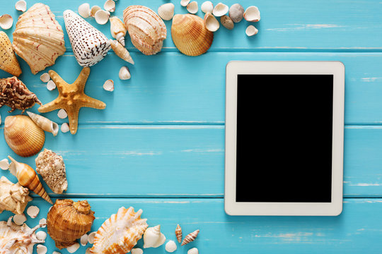 Seashells on blue wood, booking tickets on digital tablet