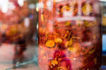 Marinated red and yellow peppers in large jars on display behind glass window