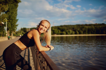 Young woman with headphones smiling at a lake in the park.