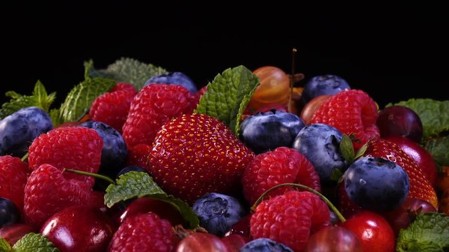 Mixed berries and mint leaves on homemade tasty pie. Close up rotation against black background. 4K.
