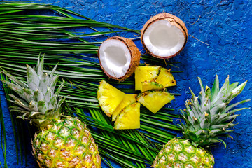 Concept of summer tropical fruits. Pineapple, coconut and palm branch on blue table background top...