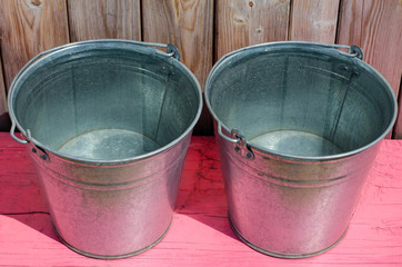 Two metal buckets of water. Pink wooden bench. Rustic wood planks background