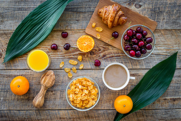 Light summer breakfast. Muesli, oranges, cherry, croissant and coffee on wooden table background top view
