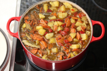 Cooking. Beef stew with potatoes, pepper and carrots in big red round casserole.
