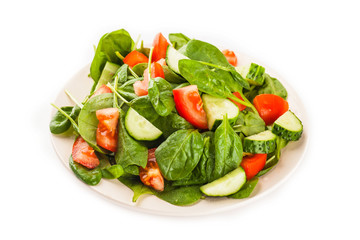 Salad with tomato, cucumber and spinach on the plate isolated on white background
