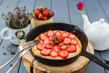 Homemade pie with fresh strawberries and whipped cream in cast iron skillet served with tea and wild thyme