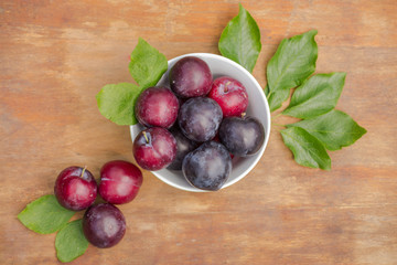 Fresh ripe plums with green leafs in a bowl on a wooden table