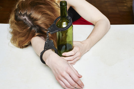 Girl asleep at a table with a bottle of wine. Female alcoholism. The symbolism of alcohol dependence.