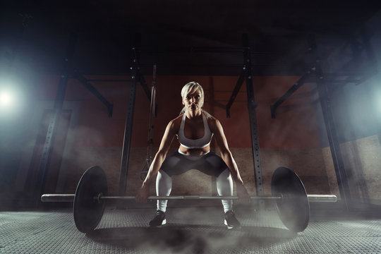 Muscular young fitness woman lifting a weight in the gym