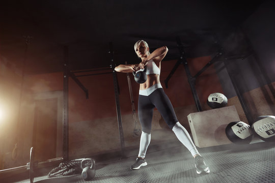 Muscular young fitness woman lifting a weight in the gym