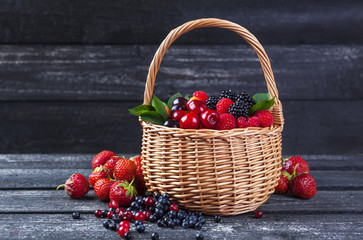 Fototapeta na wymiar Berries mix in basket on dark wooden background