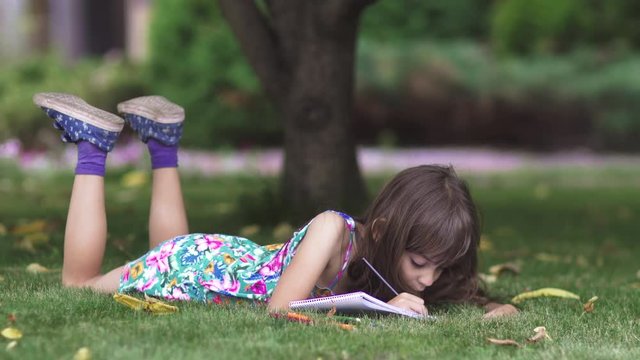 kid paint lying on the grass under a tree. little girl draw with crayons in the back yard