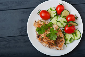 Fried chicken fillet decorated with cherry tomatoes and cucumber, top view.