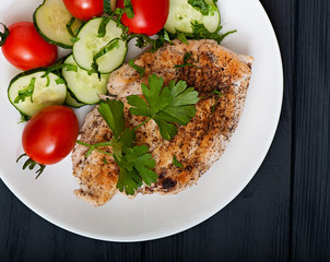 Fried chicken fillet decorated with cherry tomatoes and cucumber, top view.