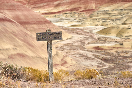 Lonely old wooden sign "Do Not Walk on Exposed Ground" with natural dried landscape on the background. Painted Hills in John Day Fossil Beds National Monument.