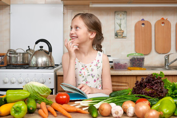 child girl with fruits and vegetables in home kitchen interior, read cooking book, healthy food concept