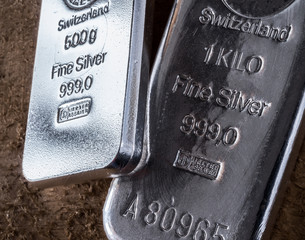 Silver bullion bars. Two fine silver bars on a.background of a rough wooden texture. .The texture of the surface of the silver ingot..