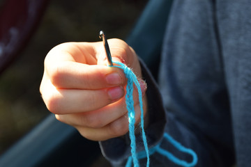 Dirty hands making a chain of blue wool on crochet