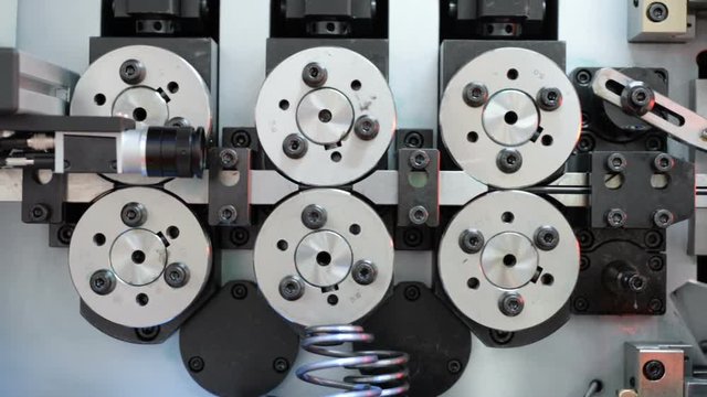 High-performance automatic machine for making steel springs. Roller wire feeder. Pan left to right.