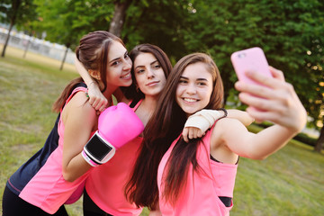 Three young pretty girls doing sports and making selfies on a smartphone