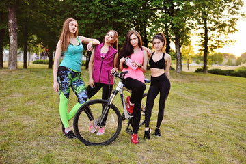 Naklejka premium Four fitness girls in a park in sportswear on a background of a bicycle and nature