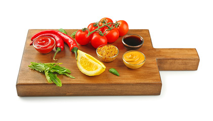 Wooden board with different sauces and vegetables on white background