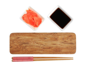 Wooden board, chopsticks, soy sauce and pickled ginger on white background