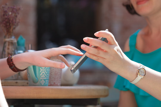 woman holds a smartphone in her hand over a table in a cafe, shows her friend a screen with a photo