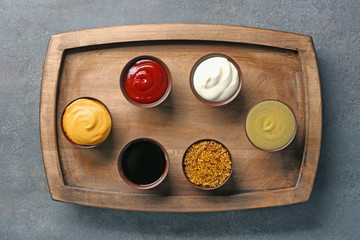 Wooden plate with different sauces on gray background