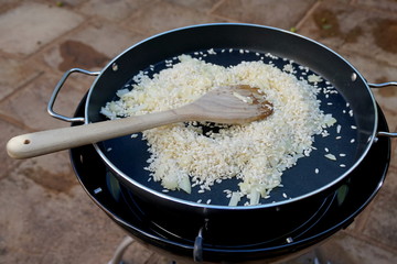 Paella rice in an outdoor cooking pan with chopped onions