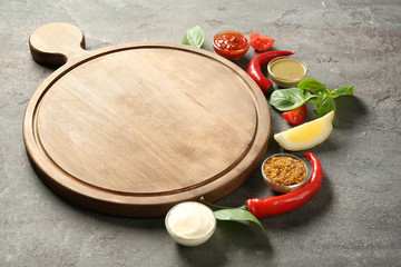 Wooden board, different sauces and vegetables on gray background