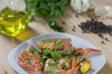 A dish of king prawns. Background: olive oil, parsley, garlic and black pepper grains.