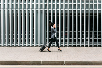Side view of young businesswoman walking with suitcase 