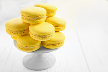 Stand with tasty lemon macarons on white wooden table, closeup