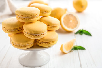 Stand with tasty lemon macarons on white wooden table, closeup