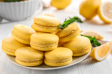 Plate with tasty lemon macarons on white wooden table, closeup