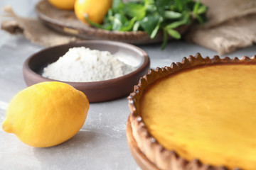 Fototapeta na wymiar Wooden plate with tasty lemon curd pie and ingredients on table, closeup