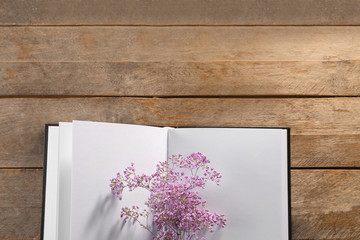 Open book with blank pages and beautiful flowers on wooden background