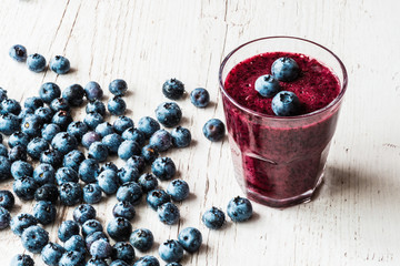 Glass of the blueberry smoothie with berries on white wooden background. Healthy drink.