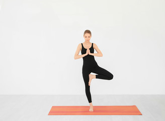 Young beautiful woman practicing yoga pose near white wall indoors